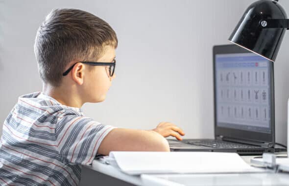 elementary-school-student-with-glasses-sits-table-with-laptop-does-his-homework-online-720x380
