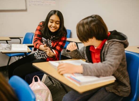 A young girl shares her mobile screen with a classmate