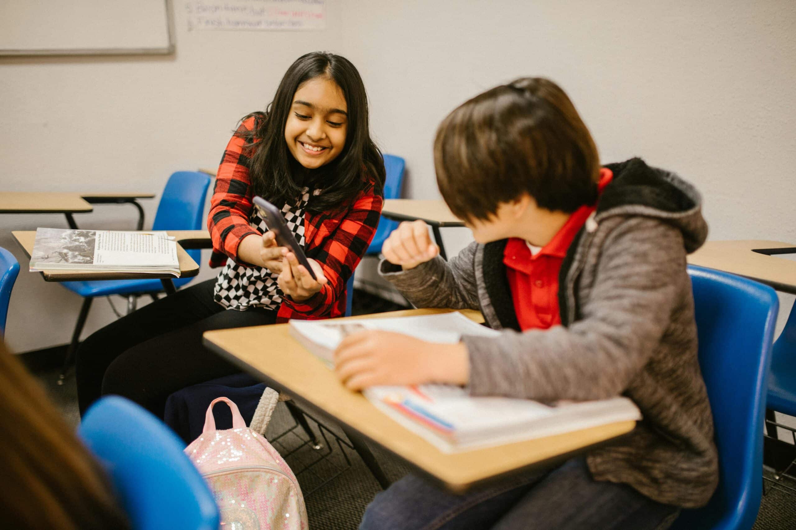 A young girl shares her mobile screen with a classmate