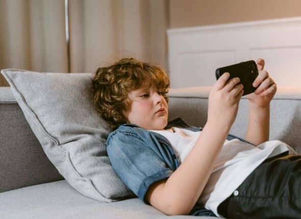 Red headed boy lying on the sofa using a mobile phone in a blue shirt