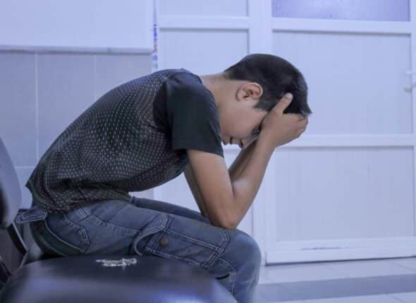 Young boy with dark hairs sits with his head in his hands