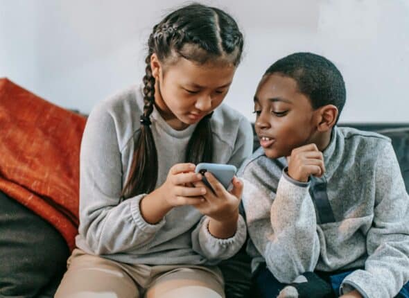 To children sitting on a sofa looking at a mobile phone.