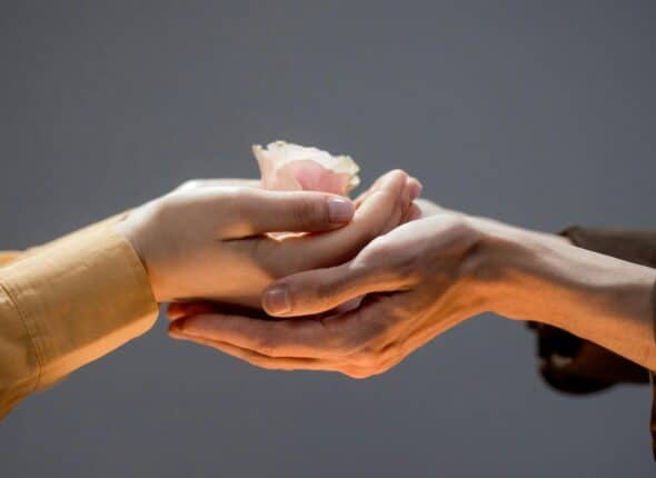 Close up of a man and woman touching hands and the woman hold a flower