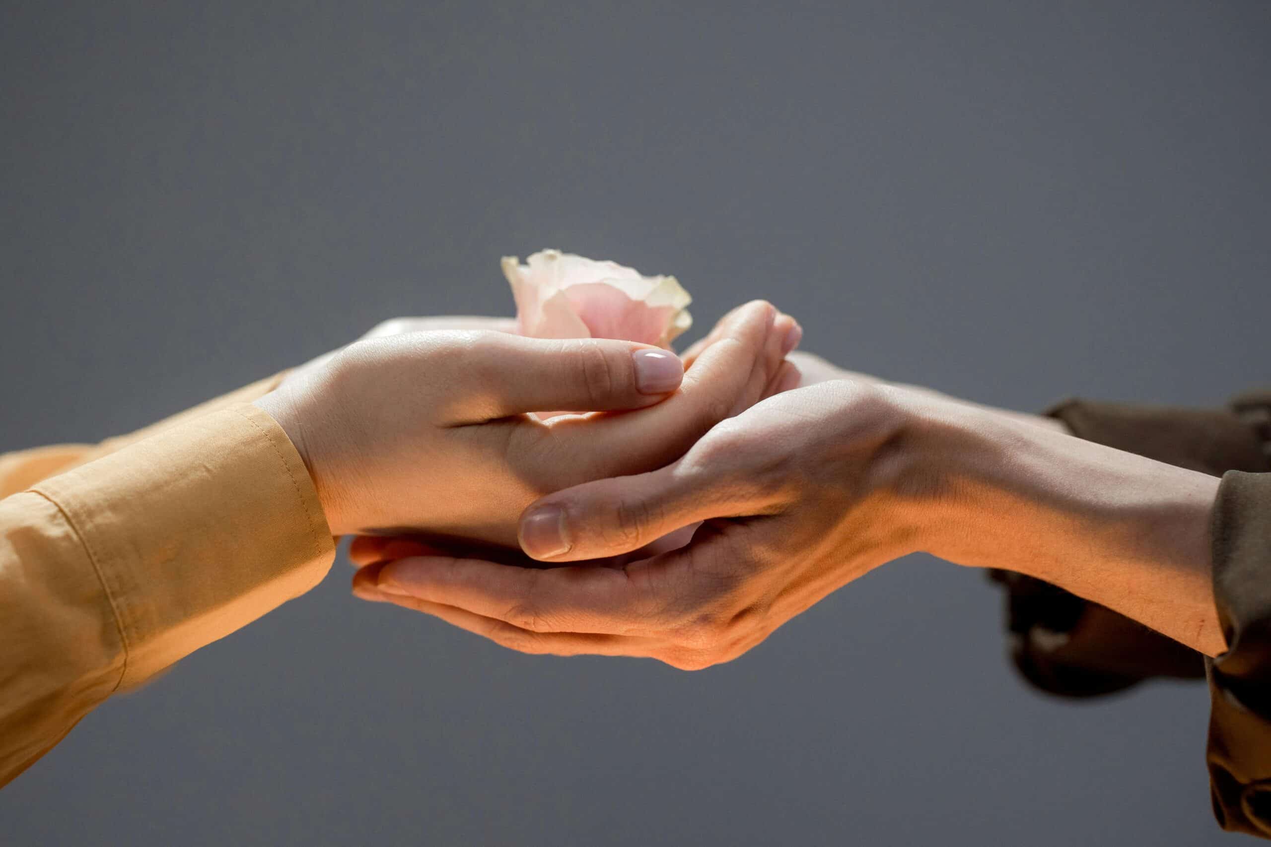 Close up of a man and woman touching hands and the woman hold a flower
