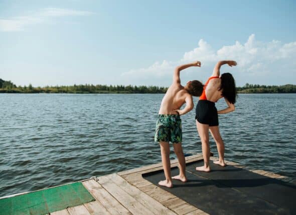 A mother and son in swimmers stretching by a lake