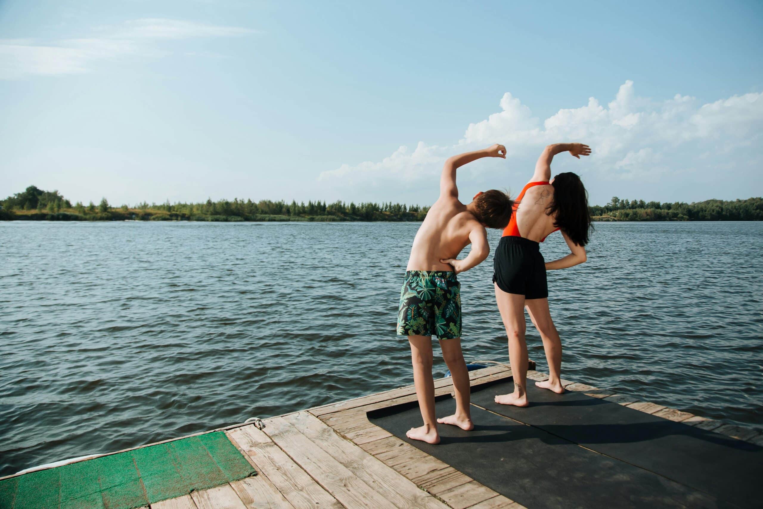 A mother and son in swimmers stretching by a lake